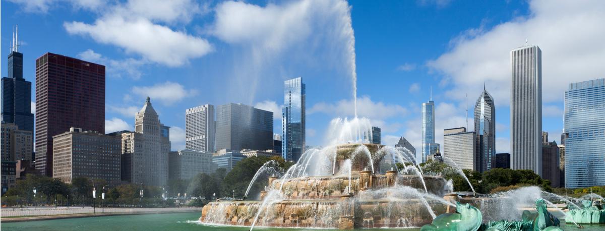 Buckingham Fountain in Grant Park with the Chicago skyline under a blue sky.